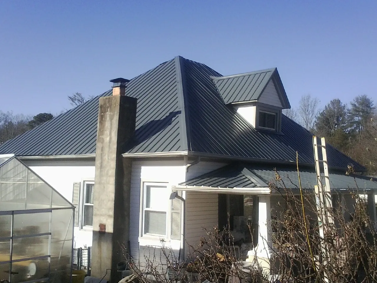 Dark blue standing seam metal roof on a white farmhouse with dormer — Slate & Tile Roof Repair by Roofing Brothers in Pewaukee