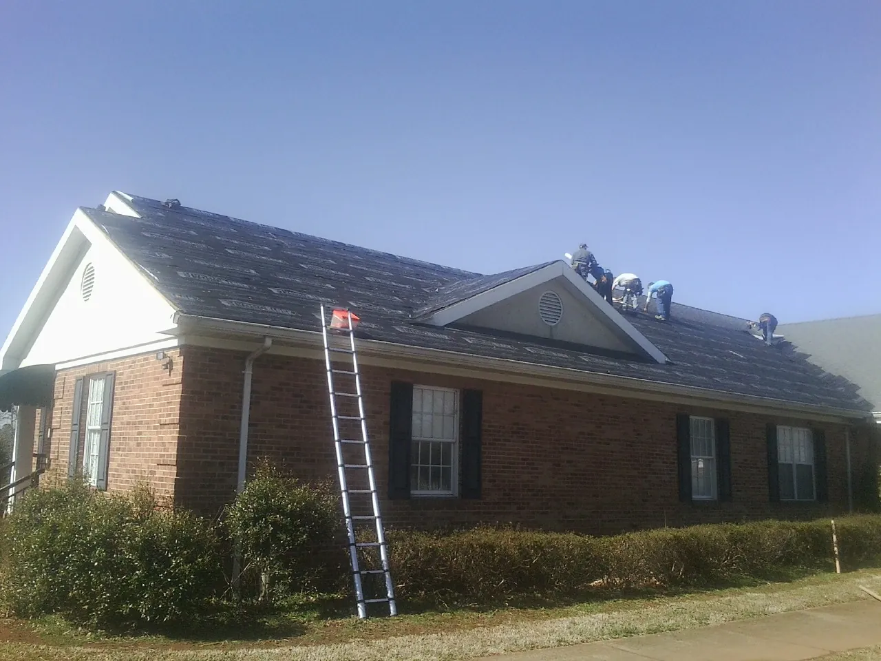 Crew tearing shingles off a brick ranch roof with a ladder set — Metal Roof Repair work by our crew in Pewaukee