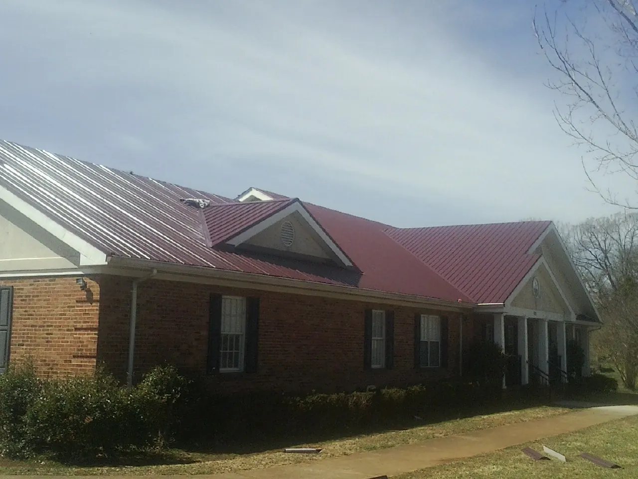 Red metal roof with gabled entries on a long brick building, from a Hail Damage Roof Repair job in Pewaukee