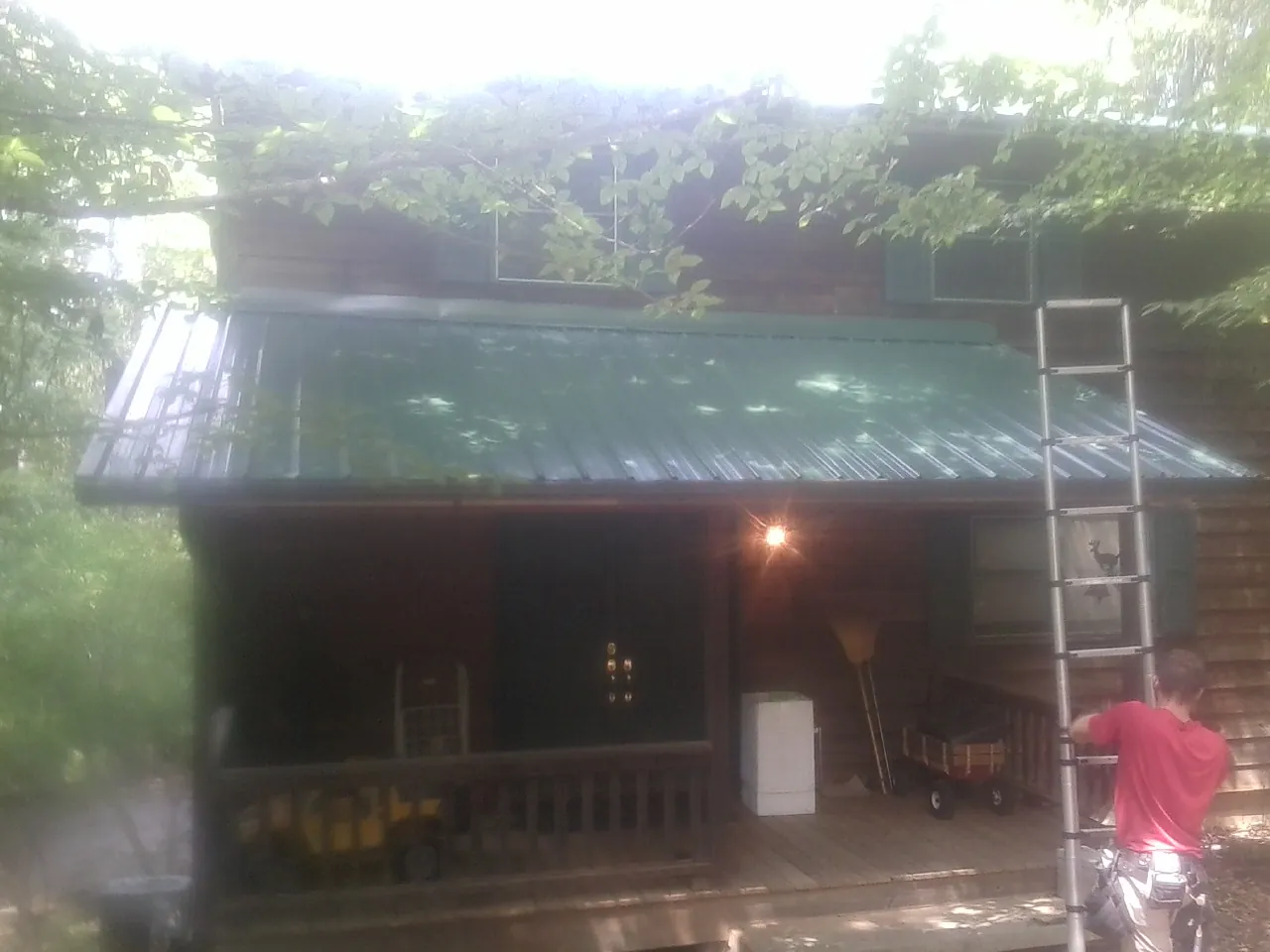 Worker on a ladder at the green porch roof of a wooded cabin in Pewaukee
