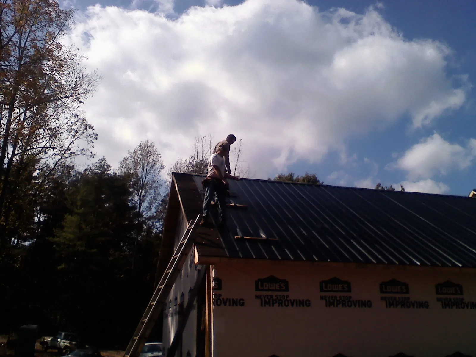 Roofer fastening dark metal panels high against a cloudy sky, from a Roof Inspection job in Pewaukee